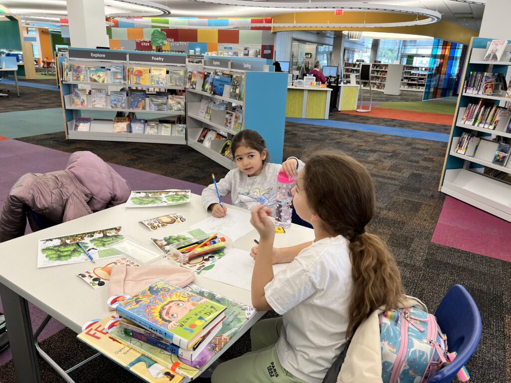 two girls are sitting at the table in the library reading books